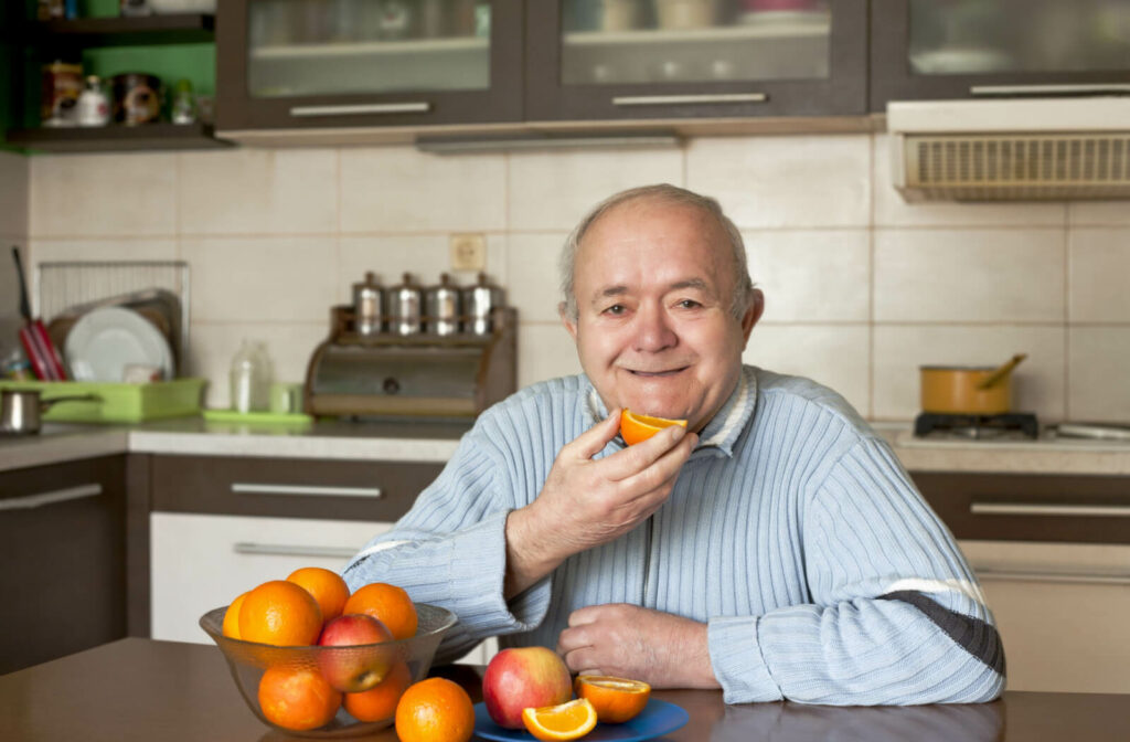 A happy older adult man eating an orange in an independent living community kitchen.
